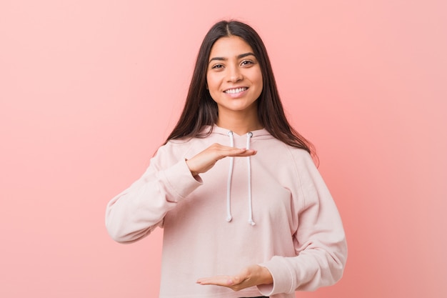 Giovane donna graziosa che indossa un look sportivo casual tenendo qualcosa con entrambe le mani, presentazione del prodotto