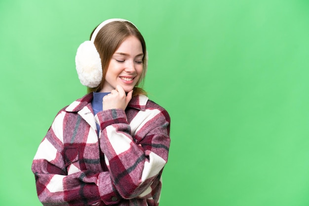 Young pretty woman wearing winter muffs over isolated chroma key background looking to the side