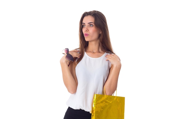 Young pretty woman in white blouse and black skirt holding dark sunglasses and shopping bag on white background in studio