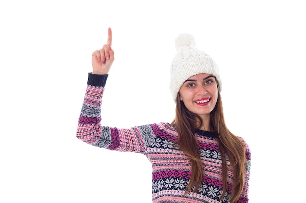 Young pretty woman in white hat and purple sweater pointing up on white background in studio