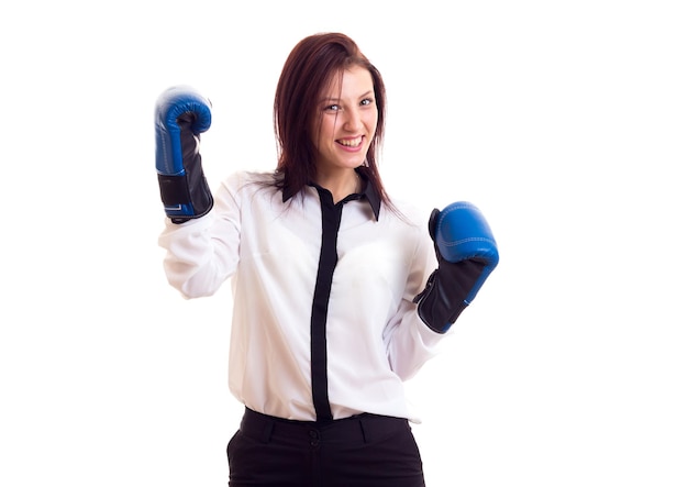 Giovane bella donna in camicia bianca e pantaloni neri con capelli scuri e guanti da boxe blu su sfondo bianco in studio