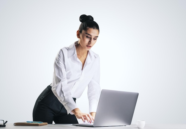 Young pretty woman in white shirt typing on modern laptop keyboard isolated on abstract light grey wall background closeup