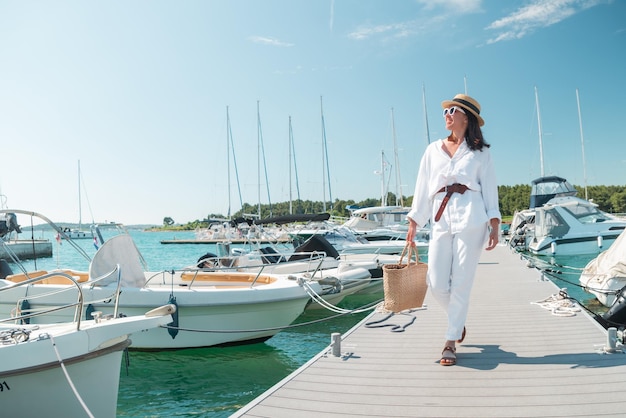 Young pretty woman in white summer clothing walking by yachts dock. copy space