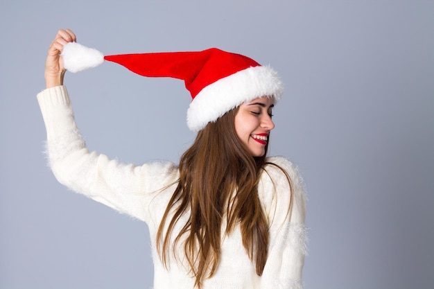 Young pretty woman in white sweater with red christmas hat holding bubo on grey background in studio