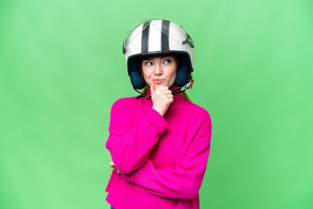 Фото Молодая красивая женщина в мотоциклетном шлеме на изолированном фоне хроматического ключа, сомневающаяся и думающая