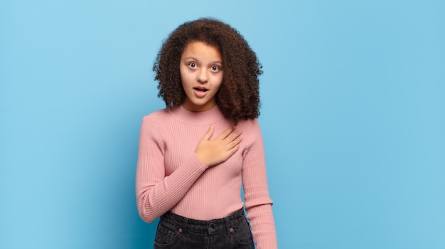 young pretty woman with afro hair and pink sweater posing on blue wall