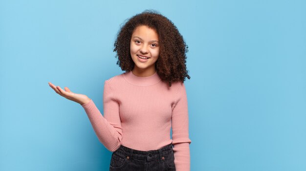 Foto giovane donna graziosa con capelli afro e maglione rosa in posa sulla parete blu