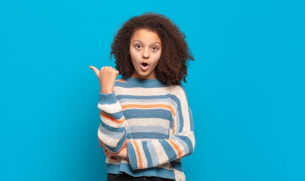 young pretty woman with afro hair and striped sweater posing on blue wall