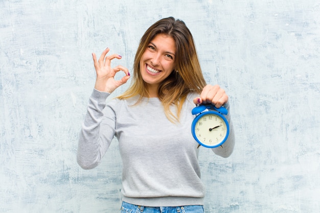 Young pretty woman with an alarm clock on grunge wall