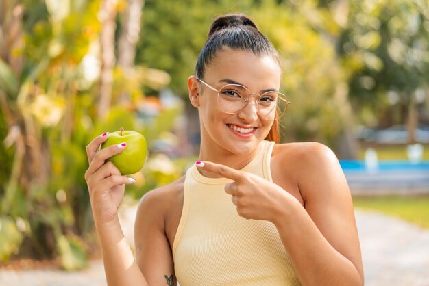 Young pretty woman with an apple at outdoors and pointing it