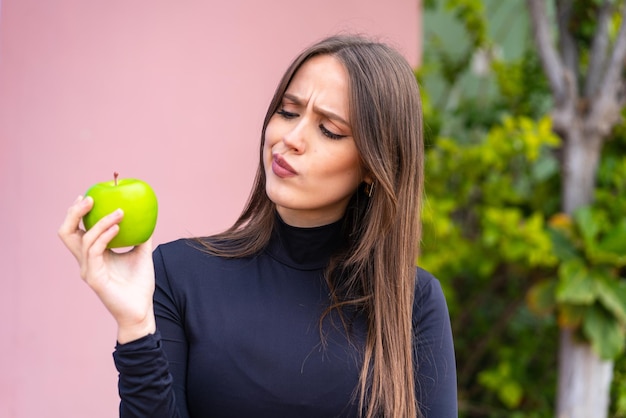 Giovane donna graziosa con una mela all'aperto con espressione triste