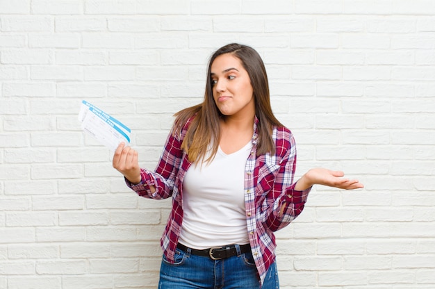 Young pretty woman with boarding pass tickets against brick wall texture