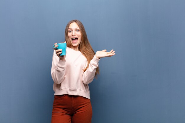 Young pretty woman with a coffee against blue wall with a copyspace