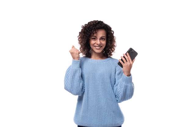 Young pretty woman with curly method hairstyle smiling holding smartphone in her hand