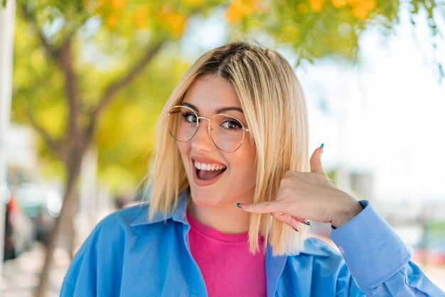 Foto giovane bella donna con occhiali all'aperto facendo il gesto del telefono chiamami segno di ritorno