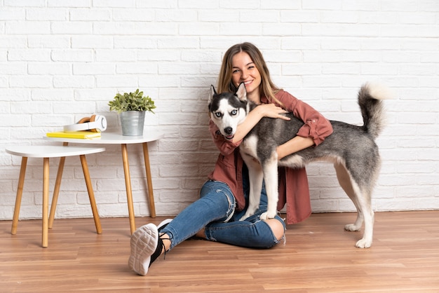 室内の床に座っている彼女のハスキー犬を持つ若いきれいな女性