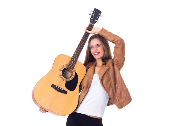 Молодая красивая женщина с длинными волосами в куртке и черных брюках держит гитару и корчит рожи