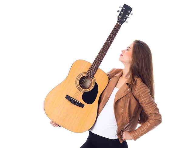 Young pretty woman with long hair in jacket and black trousers holding a guitar and making faces