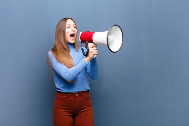 Young pretty woman with a megaphone against blue wall with a copy space