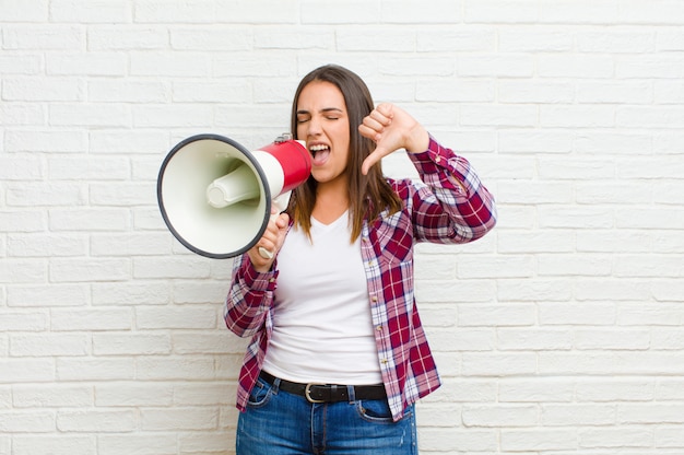 Young pretty woman with a megaphone against brick wall texture