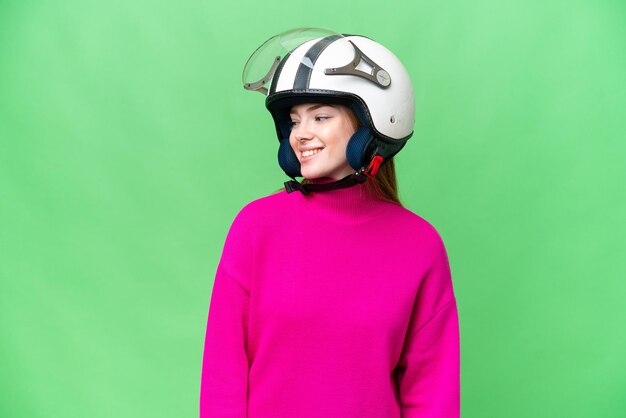 Молодая красивая женщина в мотоциклетном шлеме на изолированном фоне хроматического ключа смотрит в сторону и улыбается
