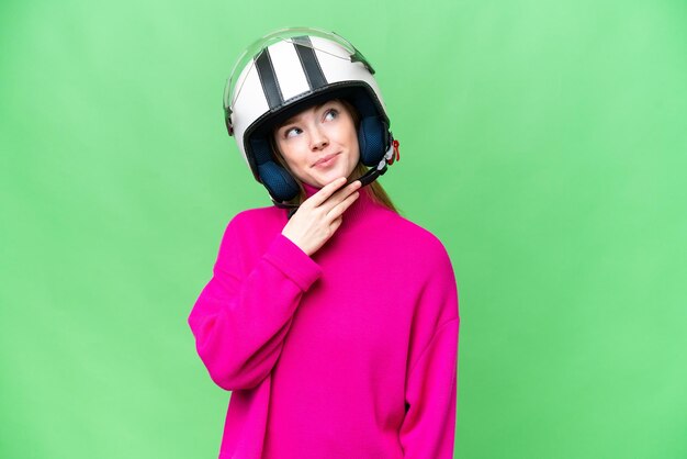 Young pretty woman with a motorcycle helmet over isolated chroma key background looking up while smiling