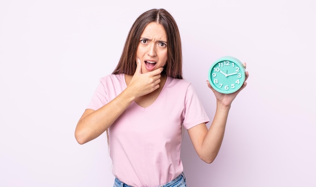 Young pretty woman with mouth and eyes wide open and hand on chin. alarm clock concept