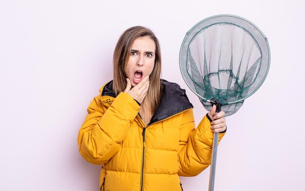 Foto giovane donna graziosa con la bocca e gli occhi spalancati e la mano sul mento. concetto di pescatore