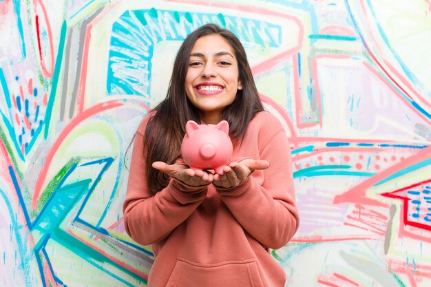 Young pretty woman with a piggy bank against graffiti wall