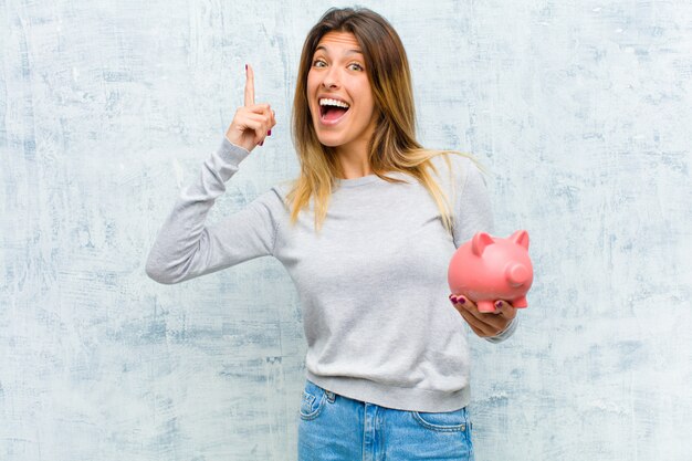 Young pretty woman with a piggy bank against grunge wall