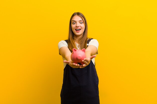 Young pretty woman with a piggy bank  against orange background