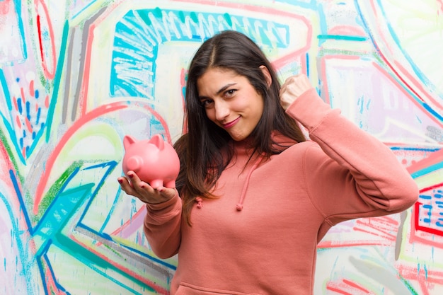 Young pretty woman with a piggy bank  graffiti wall