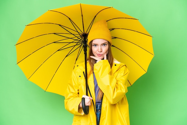 防雨コートと孤立したクロマ キー背景思考上の傘を持つ若いきれいな女性