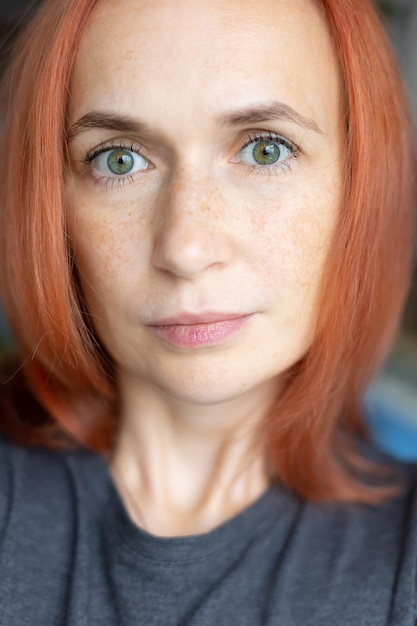 Young pretty woman with red hair green eyes and freckles looks carefully at the camera Closeup selective focus