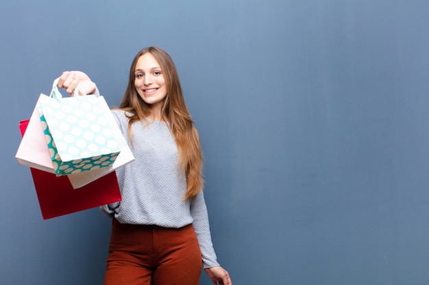 Young pretty woman with shopping bags against blue wall with a copy space