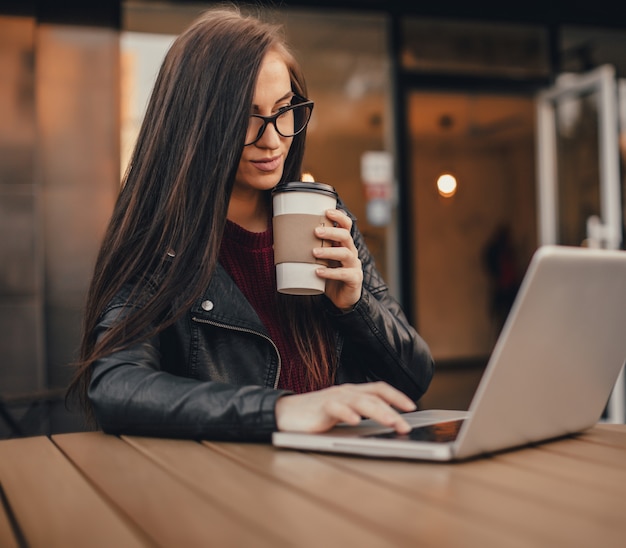 Молодая милая женщина с smartphone и чашкой кофе сидит на улице города