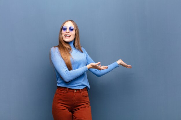 Young pretty woman with sunglasses against blue wall with a copy space