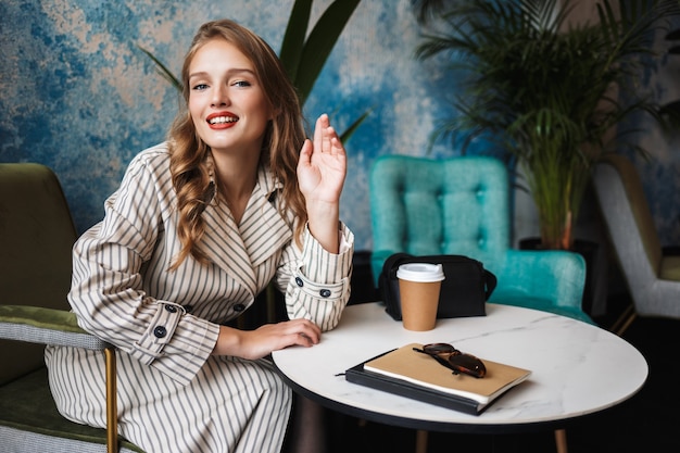 Young pretty woman with wavy hair in striped trench coat happily 