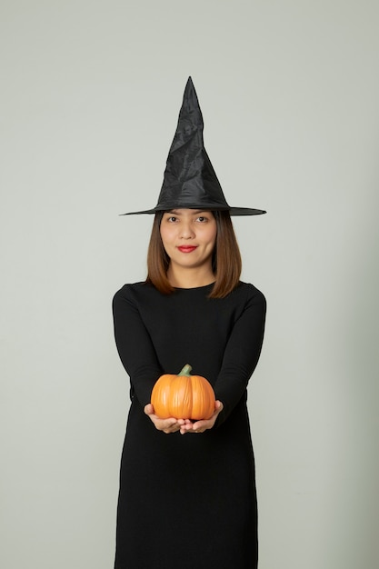 Young pretty woman with witch hat holding halloween pumpkin jack o lantern decor