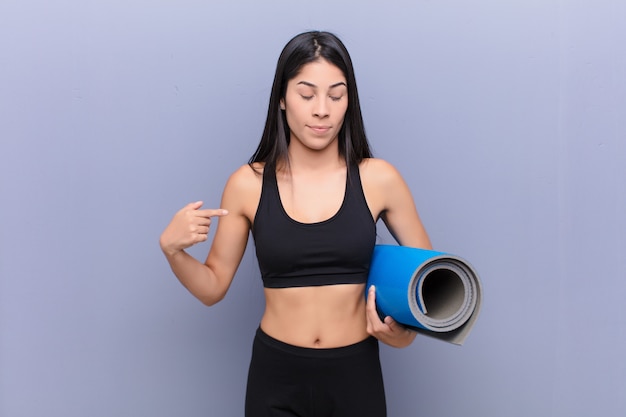 Young pretty woman with a yoga mat against cement wall