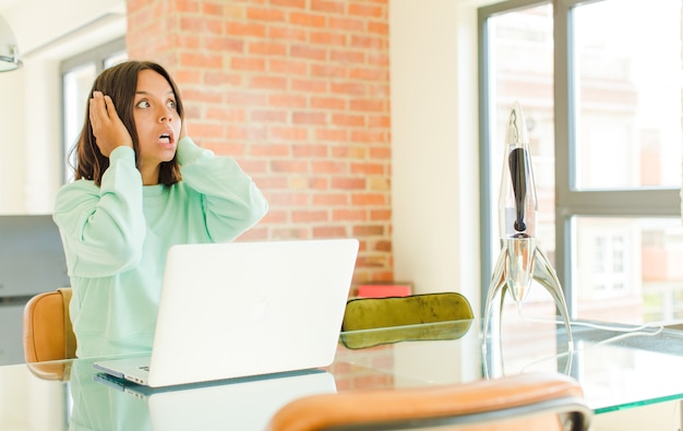 Young pretty woman working ,feeling happy, excited and surprised, looking to the side with both hands on face