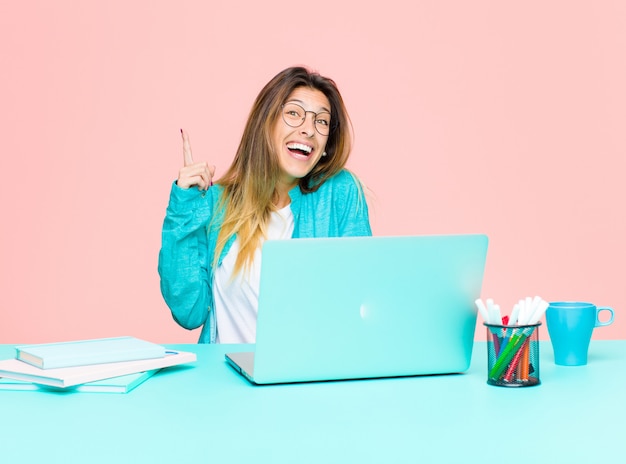 Young pretty woman working with a laptop feeling like a happy and excited genius after realizing an idea, cheerfully raising finger, eureka!