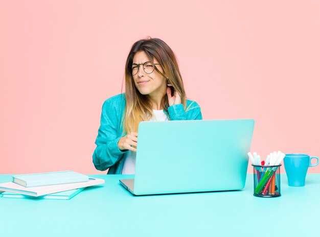 Young pretty woman working with a laptop feeling stressed, frustrated and tired, rubbing painful neck, with a worried, troubled look