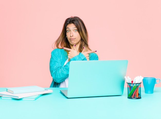 Young pretty woman working with a laptop looking puzzled and confused, insecure and pointing in opposite directions with doubts