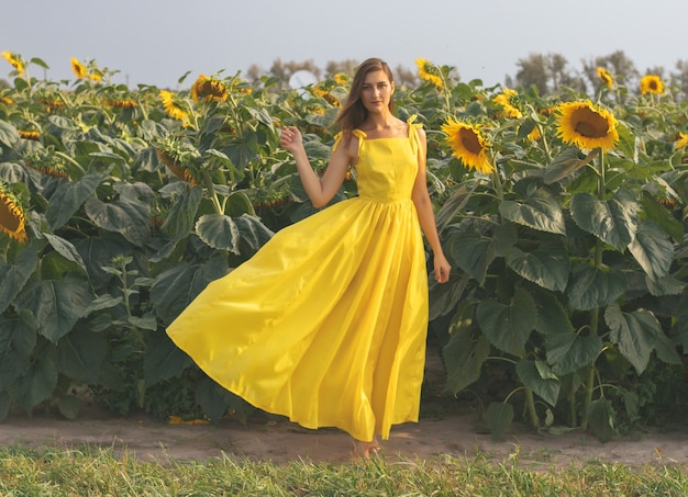 Young pretty woman in yellow dress among the field of sunflowers in summertime. Bereza, Belarus.