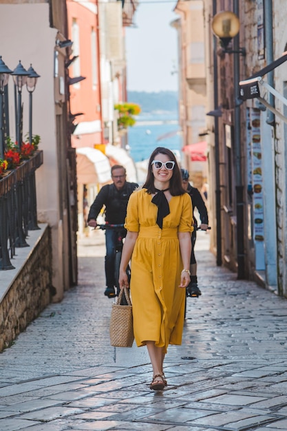 Young pretty woman in yellow dress walking by small porec city streets sea on background