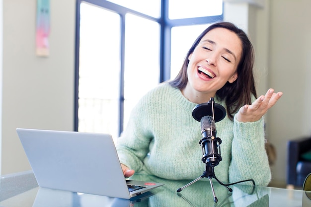 Young pretty young adult influencer woman with a microphone and a laptop on a desk