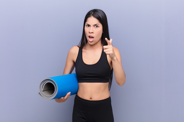 Young prettyg woman with a yoga mat against cement wall