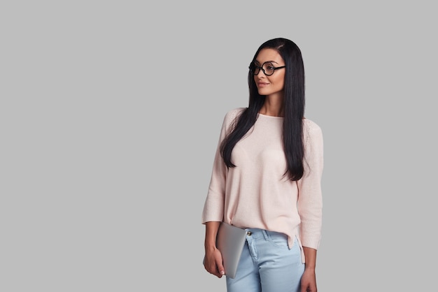 Young professional. Attractive young woman smiling and looking away while standing against grey background