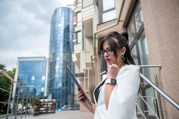 Молодая профессиональная деловая женщина в костюме, стоящая возле офисного здания со скрещенными руками